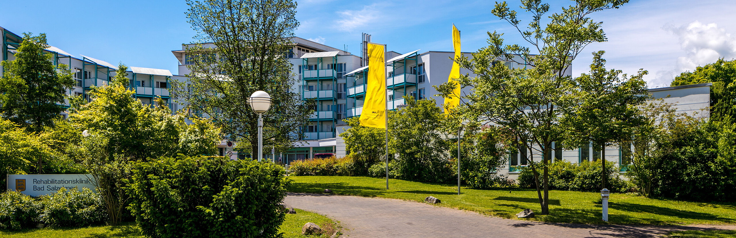 Rehabilitationsklinik Bad Salzelmen Das Bild zeigt einen gepflasterten Gehweg, der zur Rehabilitationsklinik Bad Salzelmen führt.