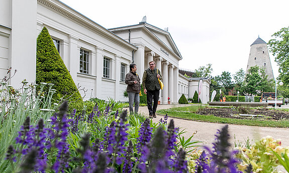 Kurpark Bad Salzelmen Zwei Personen laufen durch den Kurpark, hinter ihnen befindet sich das Lindenbad und der Soleturm.